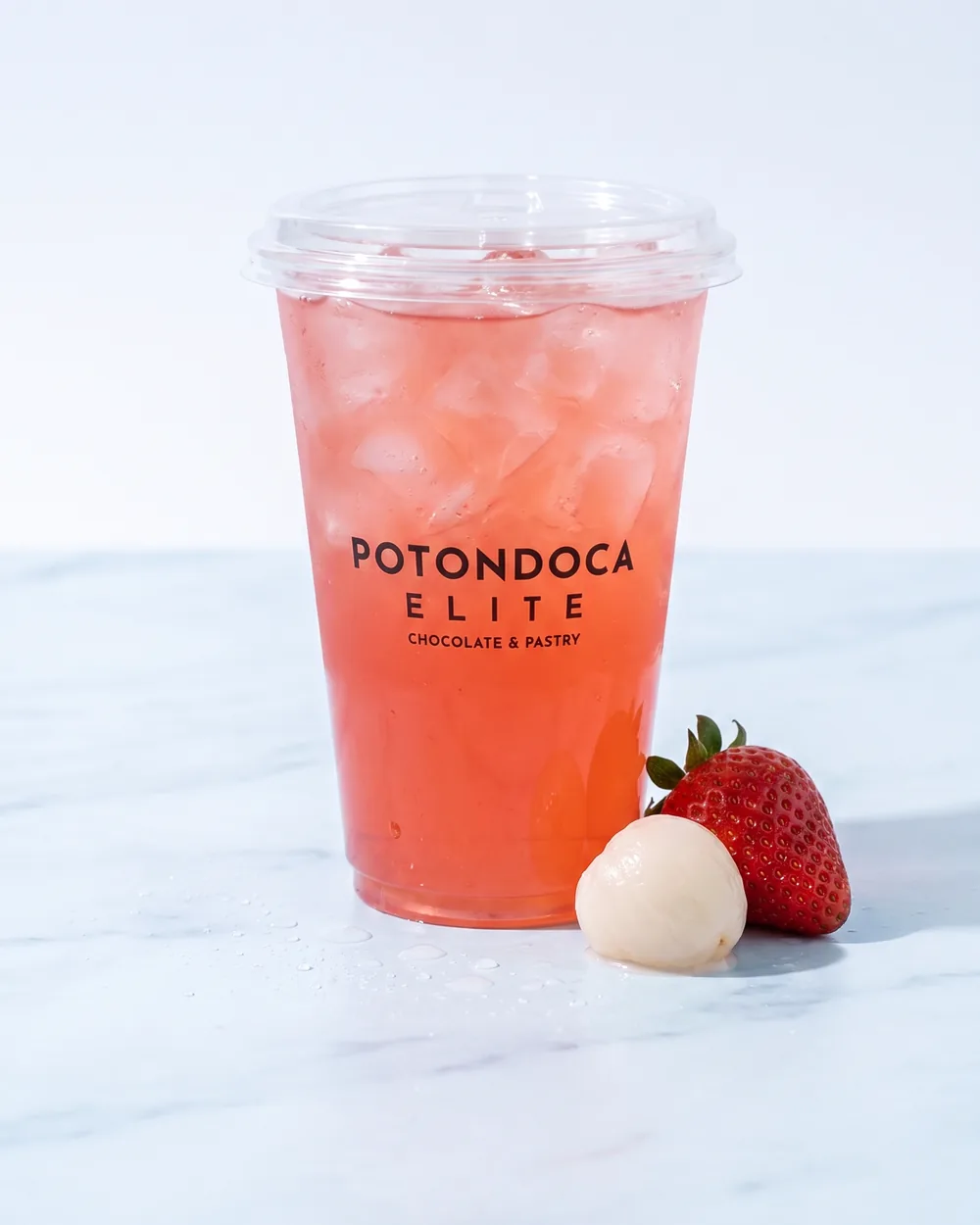 Strawberry Lychee — refresher merah muda segar dengan es di atas marmer biru muda